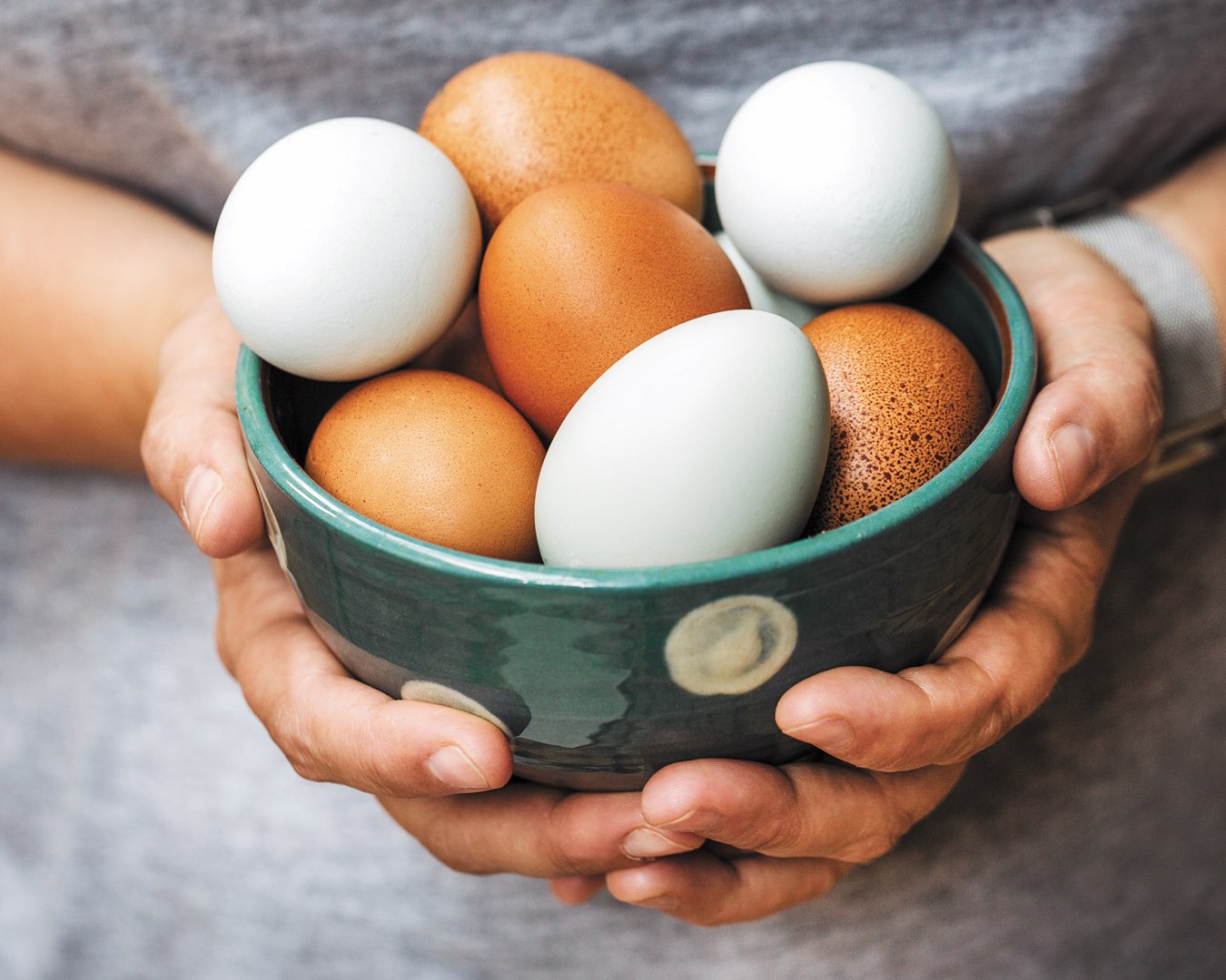 Hands holding a bowl full of brown and white eggs