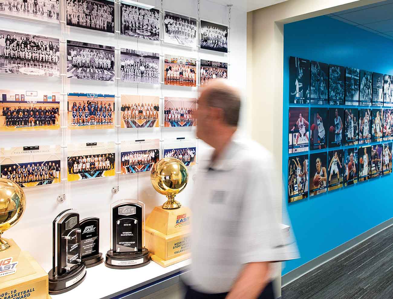 Harry Perretta walks through a hallway of trophies and team photos in Finneran Pavilion