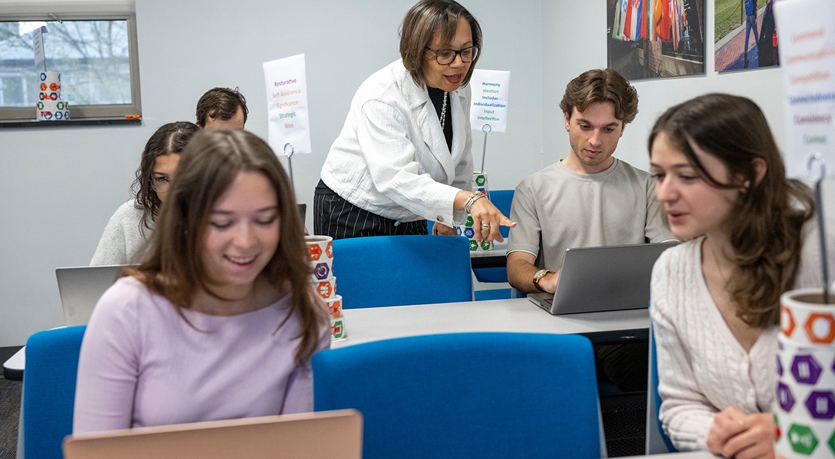 Students working together on laptops with staff member providing guidance in background