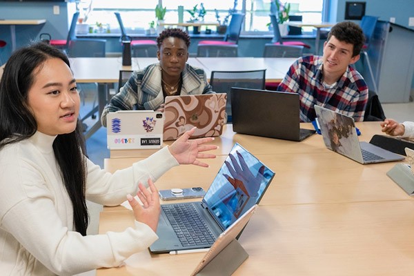 students sitting around table with laptops talking