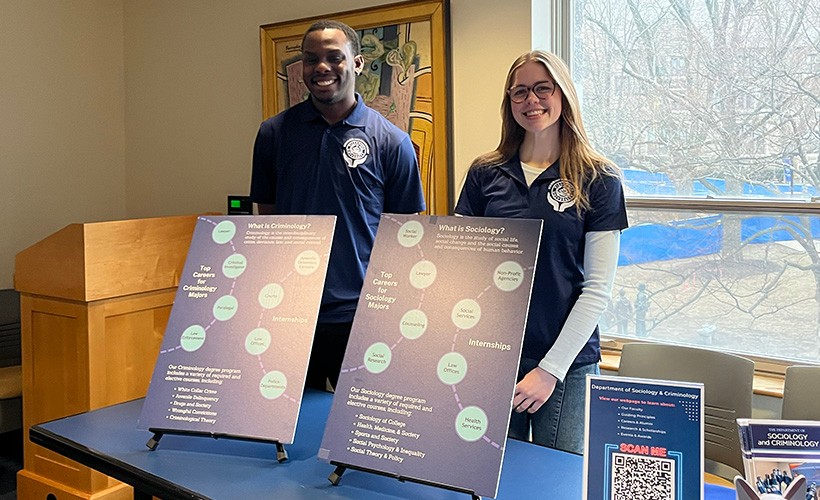 Students stand at a table behind posters about the sociology and criminology majors. Students stand at a table behind posters about the sociology and criminology majors.