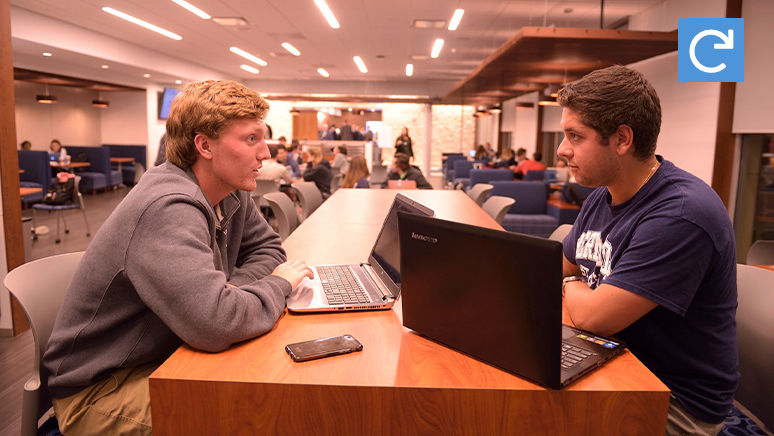 Two male stulents sitting behind the table inside of cafeteria