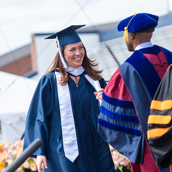 a Villanova graduate wearing a cap and gown smiles outside Villanova Stadium