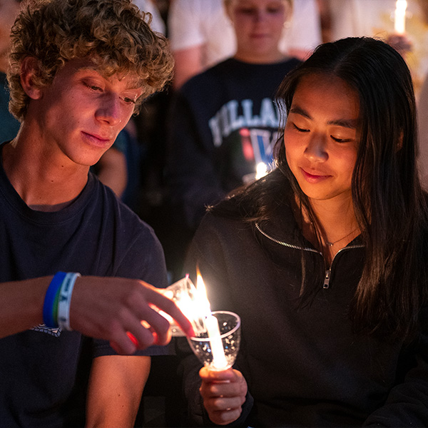 A young man lights a handle being held by a young woman. 