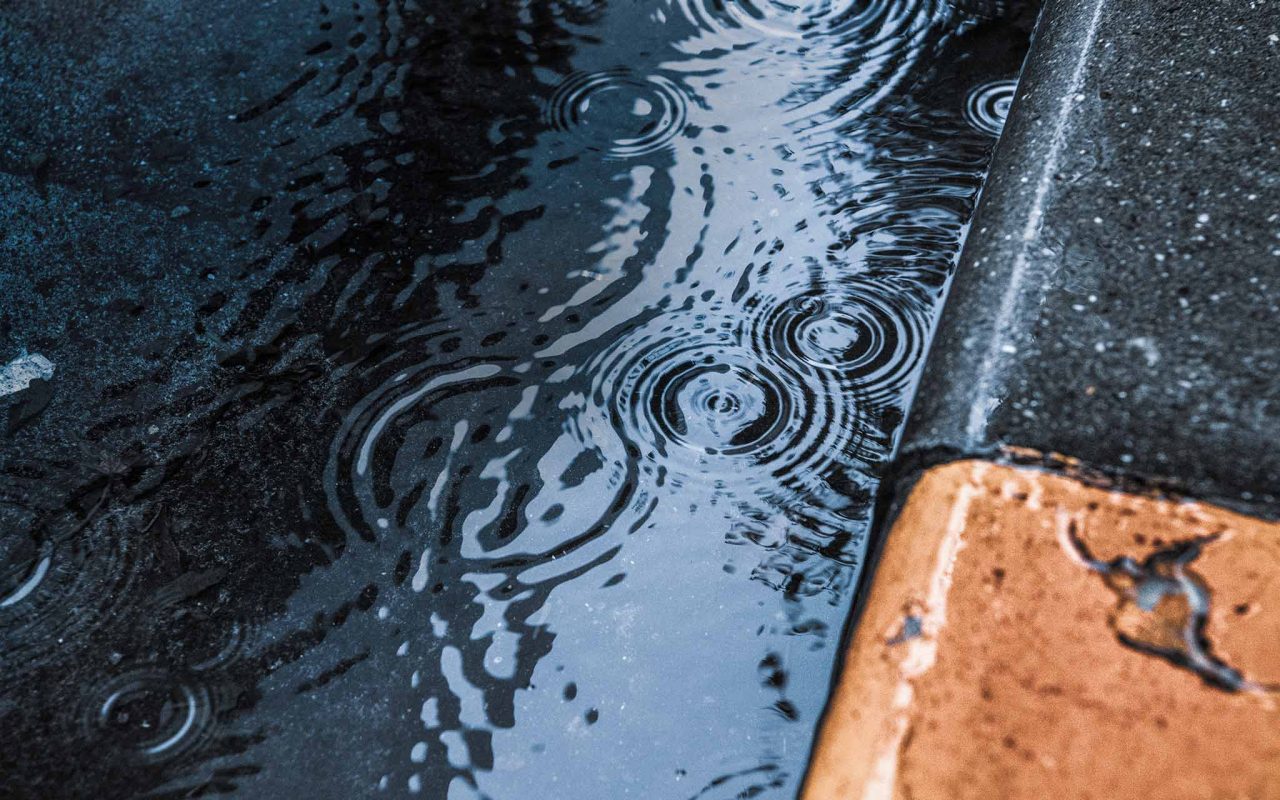 close-up of raindrops rippling in a puddle next to the street curb