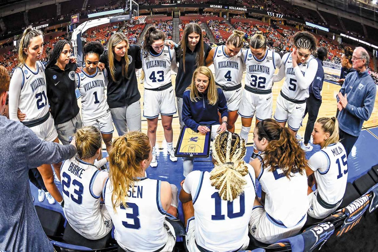 the Women's Basketball team forms a circle around Head Coach Denise Dillon